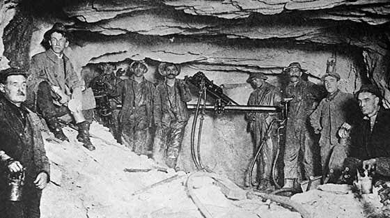 Neuf travailleurs de la construction avec leur équipement posent pour la photo en noir et blanc à l'intérieur d'un tunnel.