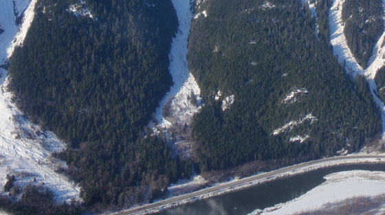 Photo d'une vue aérienne en couleur d'un secteur d'autoroute bordé de 3 couloirs d'avalanche en hiver.