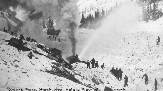 Black and white photograph of 20+ rescuers and rotary plough clearing avalanche debris.